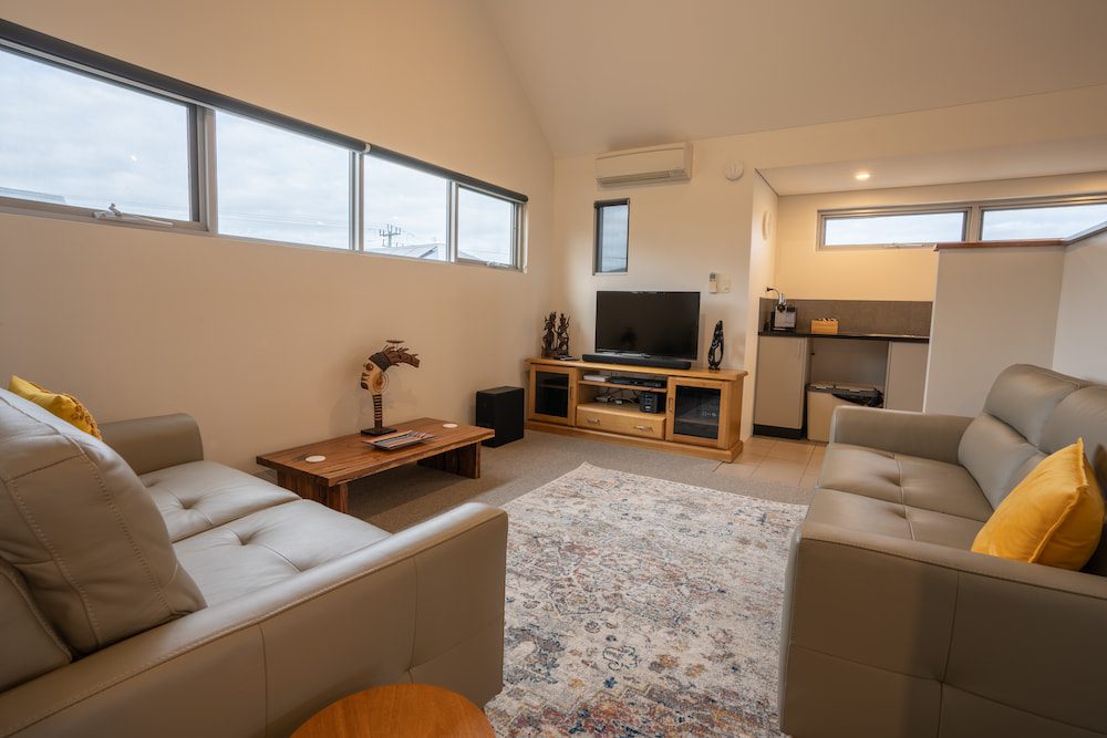 The carpeted lounge area of the Lockyer Apartment with a coffee table, TV and two leather couches.