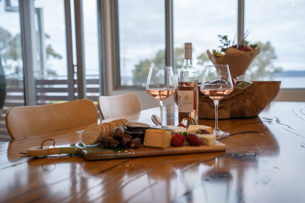 A cheese platter and two glasses of rose on the table with the view of the harbour in the background.